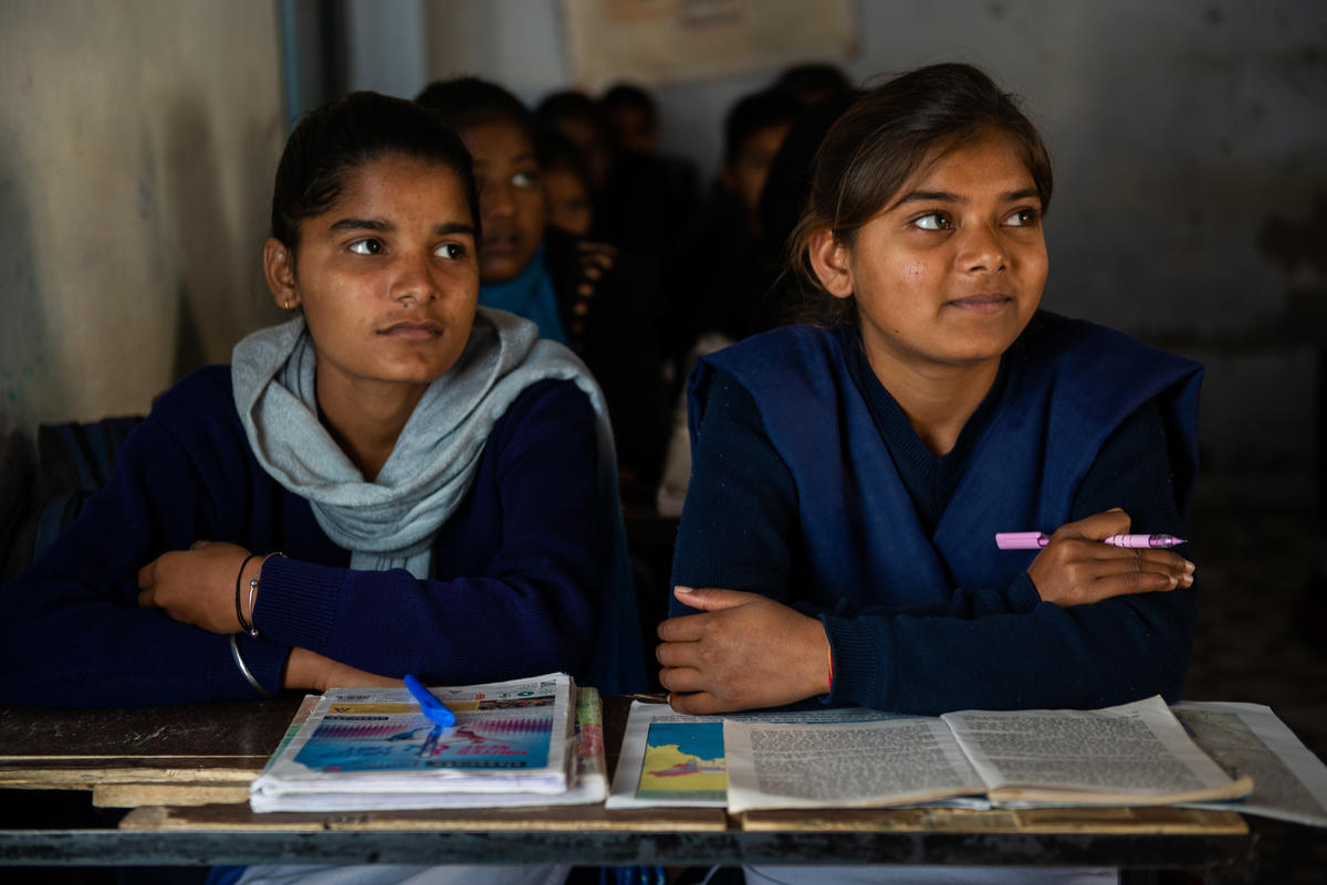 Dos colegialas de la India con uniforme escolar sentadas en un pupitre en la escuela y sonriendo