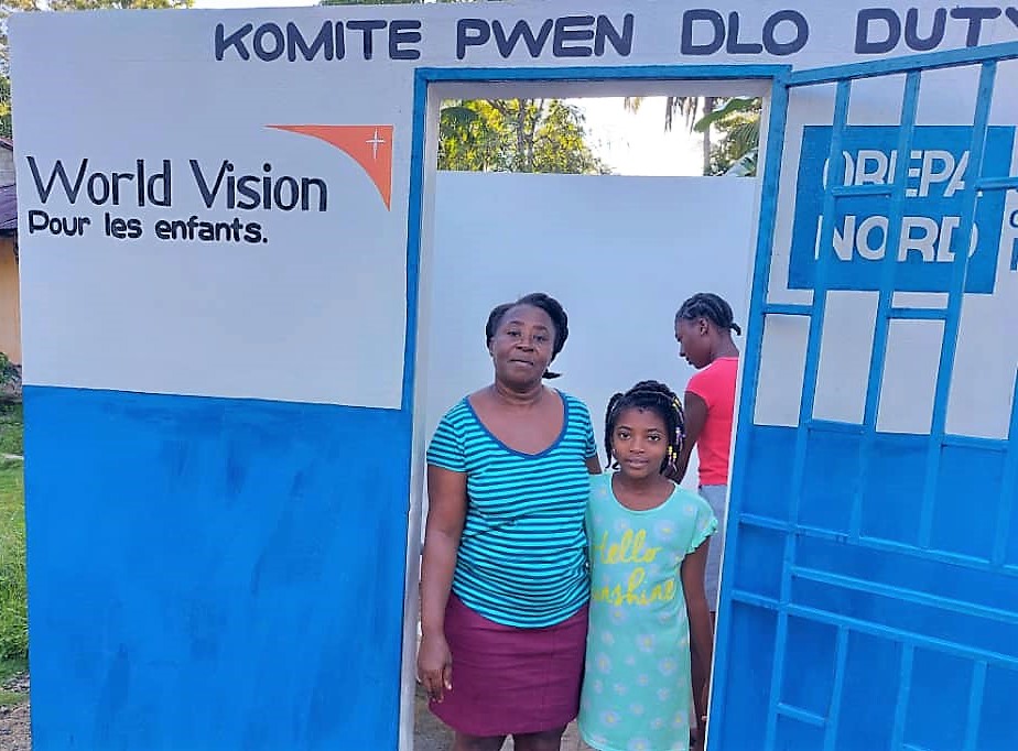 Una niña y dos mujeres de Malawi de pie en la entrada de un baño público, construido por World Vision