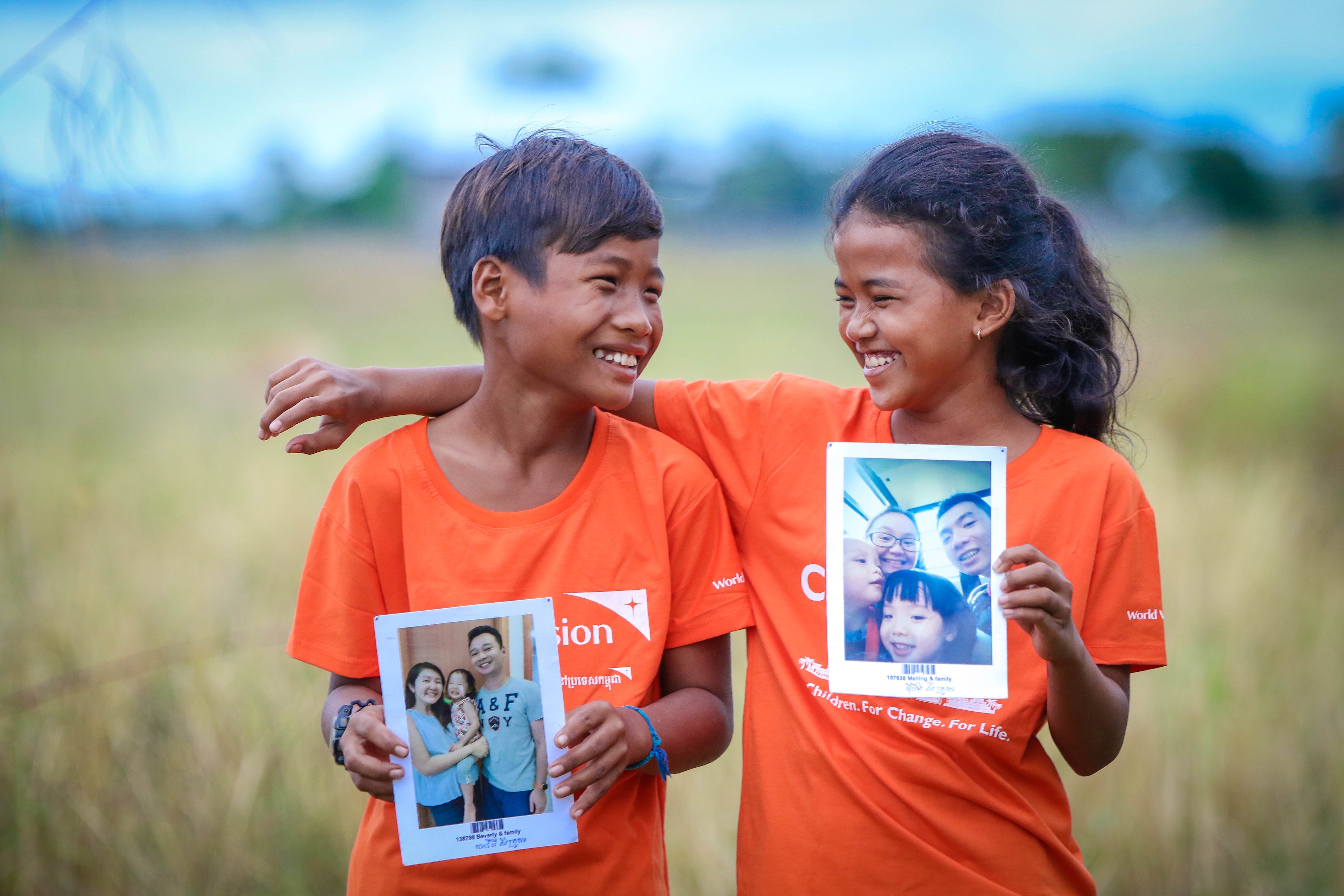 Un niño y una niña de Camboya sostienen las fotos de sus patrocinadores y se sonríen mutuamente.