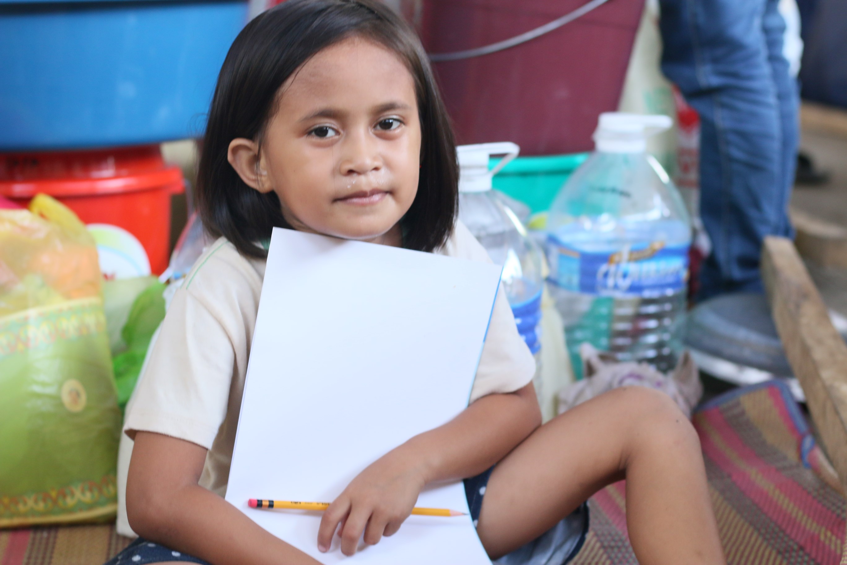 Princess mira a la cámara mientras sostiene un lápiz y un papel dentro de un centro de evacuación en Filipinas.