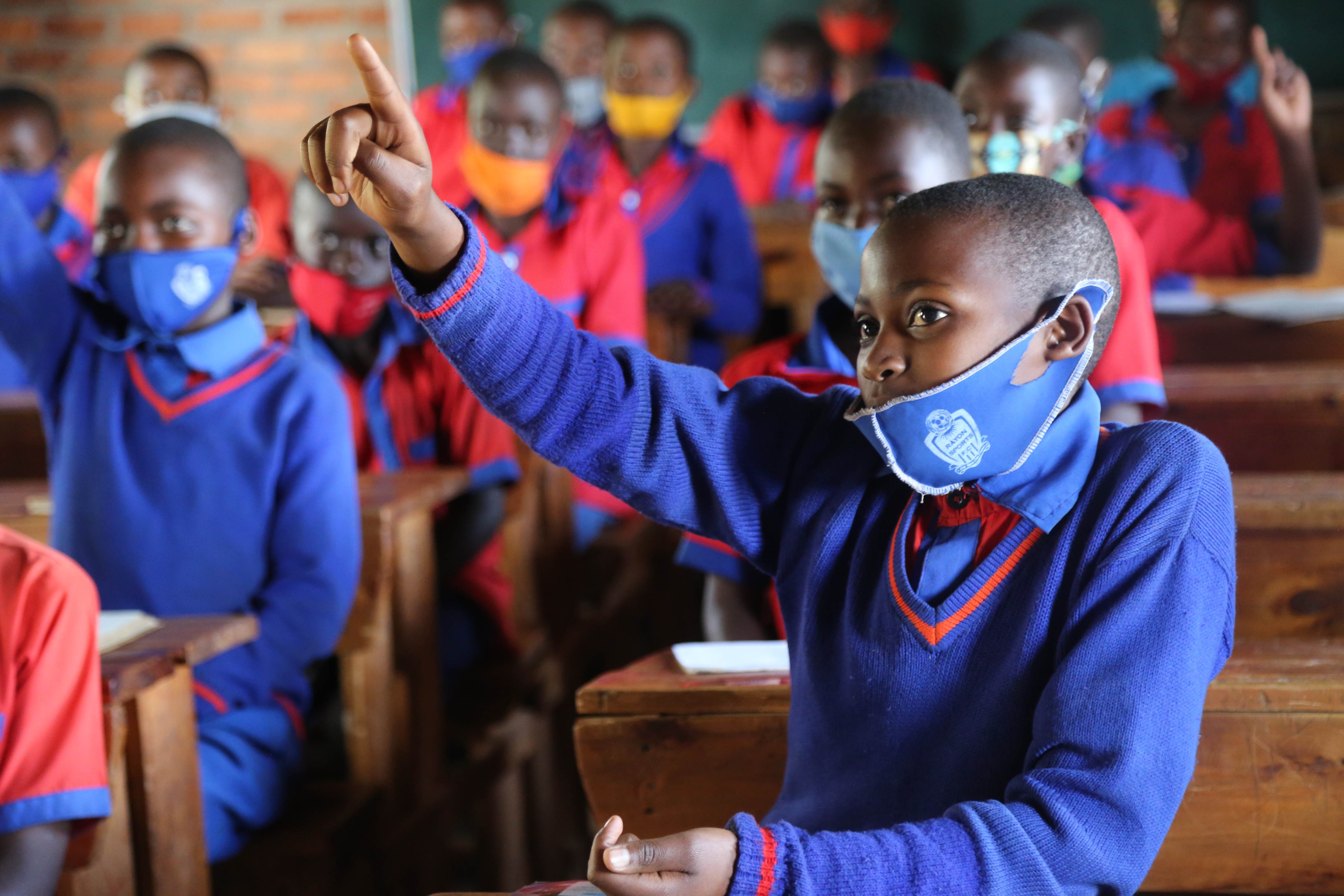Escolares con uniformes azules y mascarillas en Ruanda levantando la mano en clase